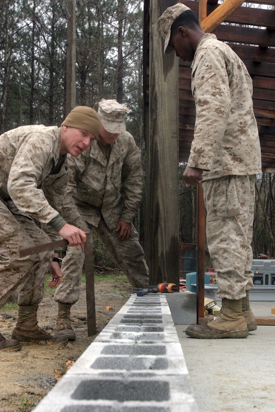 Sergeant Matthew Dike, combat engineers section head with Combat Logistics Battalion 26, advises Lance Cpl. Ethan Tobias and Cpl. Larry Pearson as they lay the first row of blocks for a new pistol rangehouse for the Blackstone Police Department in Blackstone, Va., March 31, 2008. Marines from CLB-26, the combat logistics element of the 26th Marine Expeditionary Unit, endured cold and rain for the project, which helped the Blackstone community and sharpened their own skills. The 26th MEU is conducting unit training here to prepare its Marines and sailors for a planned deployment later this year.