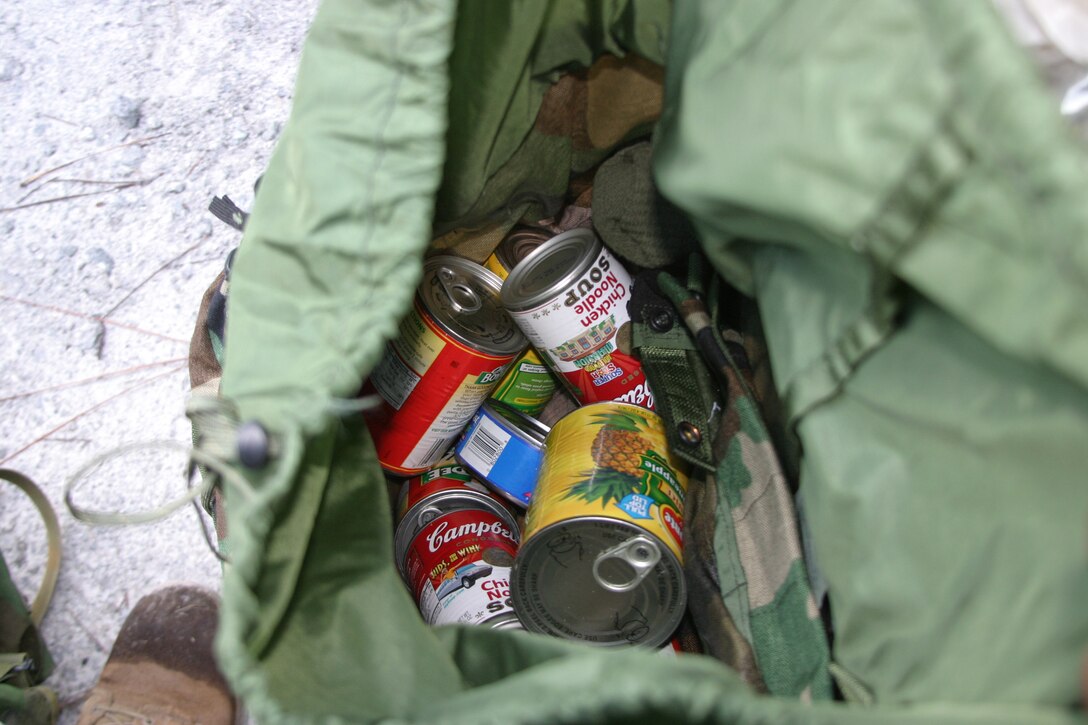 A Marine with MSSG-24 opens his pack to show the amount of food he was donating to needy families.::n::The amount of food the Marines had to carry depended on their rank.  Junior enlisted Marines and sailors had to carry 20 pounds of food.  NCO’s had to carry 25 pounds of food.  Staff Noncommissioned officers and officers had to carry 30 pounds.  The commanding officer, executive officer and sergeant major each carried 40 pounds of food.::n::Marines from MSSG-24 recently participated in an 8-mile hike and were allowed to replace their normal pack contents with a food donation for needy families in the area.::n::