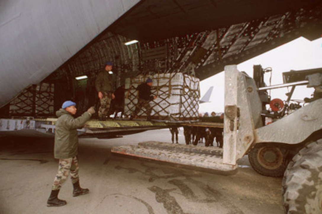 A NATO ground crew man directs a forklift as they unload pallets of kerosene and wood chips from a C-17 Globemaster III aircraft at the Sarajevo airport on Dec. 8, 1995. The humanitarian cargo was flown into Sarajevo as part of Operation Provide Promise. The Globemaster III belongs to the 437th Air Lift Wing, Charleston Air Force Base, S.C. 