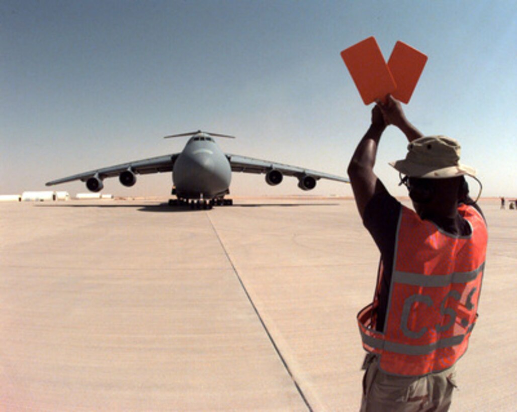 Staff Sgt. James Larose marshals a U.S. Air Force C-5B Galaxy to a parking spot on the ramp at Prince Sultan Air Base at Al Kharj, Saudi Arabia, on August 7, 1996. The Galaxy is bringing in engineers, equipment and supplies to construct a tent city to house U.S. personnel conducting Operation Southern Watch. Nearly 4,000 personnel, aircraft, and equipment are being moved from bases in Dhahran and Riyadh to the remote desert air base to reduce their vulnerability to terrorist attack. Southern Watch is the U.S. and coalition enforcement of the no-fly-zone over Southern Iraq. Larose is attached to the 615th Air Mobility Maintenance Squadron, Travis Air Force Base, Calif. 