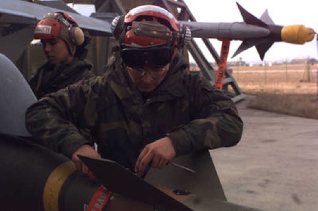 U.S. Marine Sgt. Rene R. Benedit (foreground) and Lance Cpl. Ricardo Almaguer (background) load a GBU-15 bomb onto a Marine F/A-18 Hornet at Aviano Air Base, Italy, as it is prepared for a mission over Bosnia and Herzegovina on Dec. 28, 1995. The Hornet's mission is in support of the NATO Implementation Force (IFOR) in Operation Joint Endeavor. The Marines and their aircraft are deployed to Aviano from Fighter Attack (All Weather) Squadron 224 of Beaufort, S.C. 