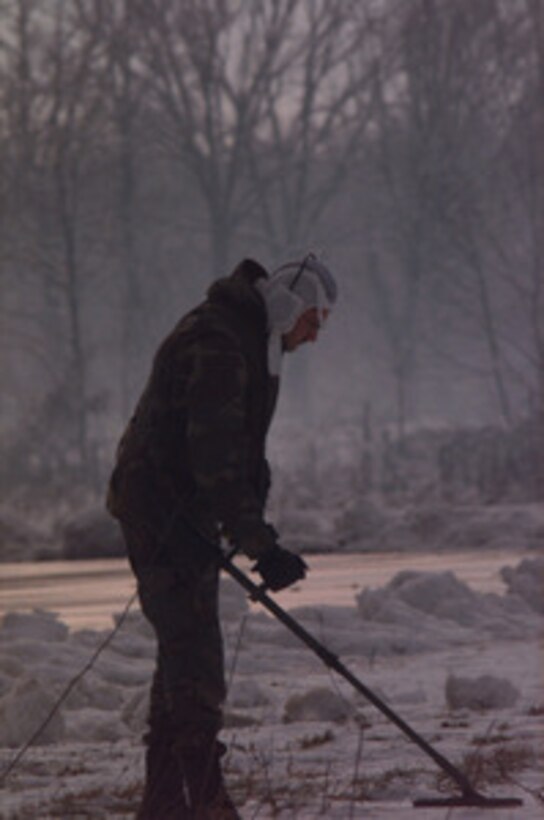 An explosive ordinance technician with the 52nd Civil Engineering Squadron, Explosive Ordinance Disposal unit, Spangdahlem Air Base, Germany, sweeps a path to a suspected anti-vehicle mine at the Tuzla Air Base in Bosnia and Herzegovina, on Dec. 31, 1995. The suspected mine was determined to be a harmless ammunition casing lid. 