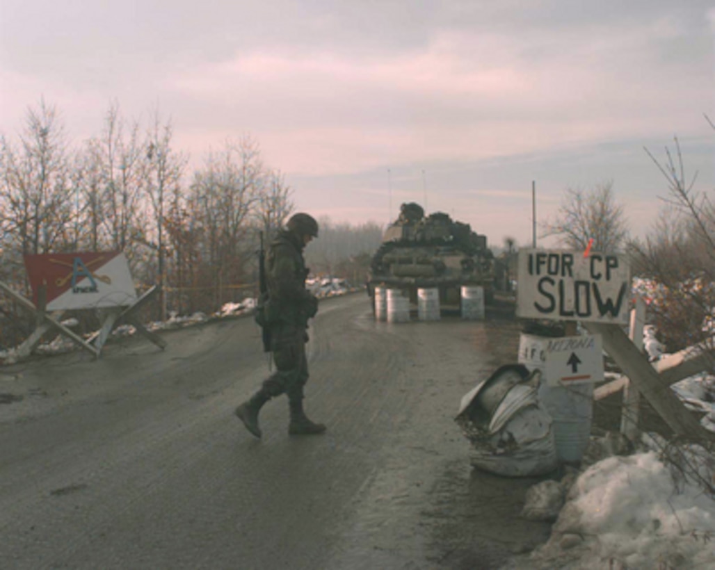 A U.S. Army scout from the 1st Cavalry crosses the road at a check point on Route Arizona in Bosnia and Herzegovina on Jan. 10, 1996. Route Arizona is the main deployment route from the Sava River Bridge for the NATO Implementation Force (IFOR) deployment into Bosnia and Herzegovina for Operation Joint Endeavor. 