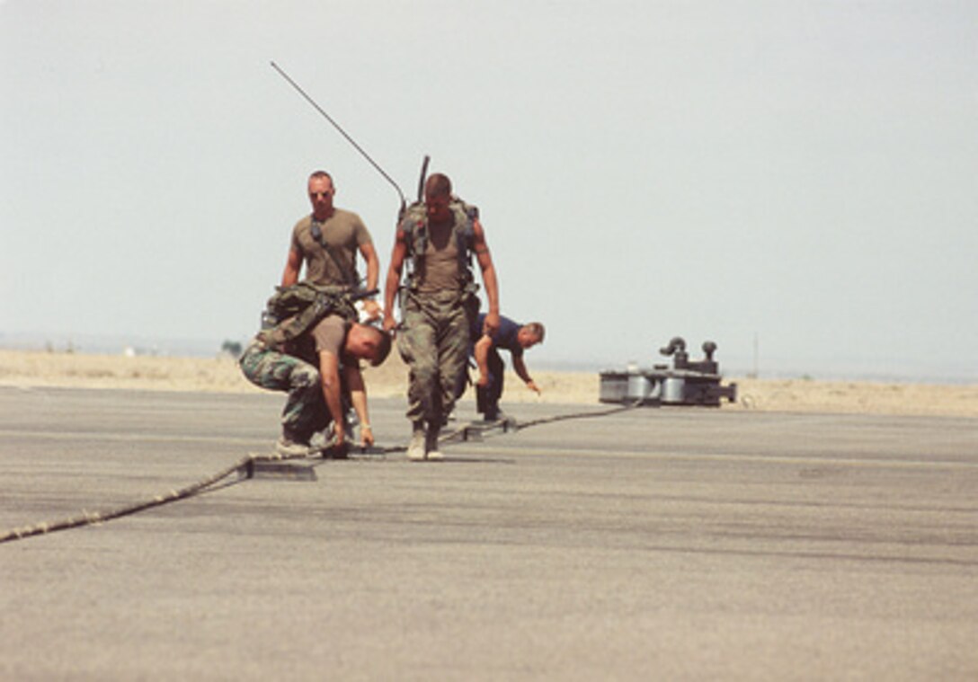 U.S. Marine expeditionary airfield technicians place boots under the cable of the M21 Arresting Gear stretched across the runway at Roswell Industrial Air Center, N.M., on June 8, 1996, as they prepare to trap a F/A-18 Hornet. The Marines are deployed from the MWSS 273, Beaufort, S.C., to Roswell for exercise Rovings Sands '96, the world's largest joint, tactical air defense exercise involving service men and women from the U.S., Germany, the Netherlands and Canada. The exercise allows multinational forces to practice tactics, techniques and procedures improving their defense capabilities. The boots lift the cable off the runway so the tailhook of the aircraft engages. 