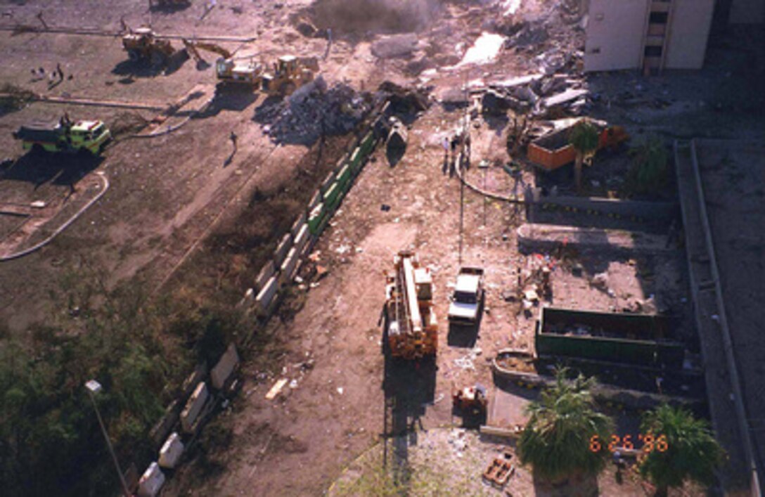 The crater caused by the explosion of a fuel truck outside Khobar Towers on Tuesday, June 25, 1996, is visible at the top of this photograph of the facility taken from a nearby building on King Abdul Aziz Air Base near Dhahran, Saudi Arabia, on June 26, 1996. The dotted line running diagonally through the photo is the concrete barrier, sometimes known as a Jersey Wall, which is credited for deflecting the blast of the explosion upward and reducing its effect. 