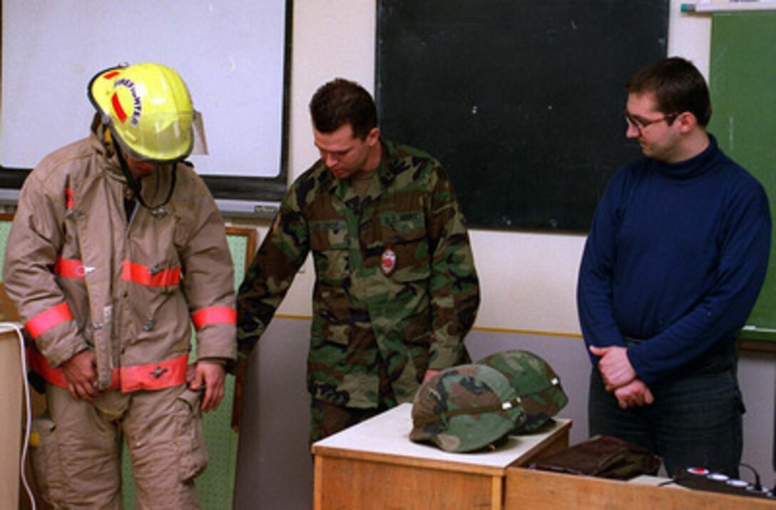 Specialist David Bishop (center) and Specialist Stacey Benedik (left), reserve fire fighters from the 487th Engineer Battalion, from Washington, Kansas, demonstrate to Hungarian students and their teacher (right) in a local school the proper way to wear a fire fighters suit. The fire fighters are stationed in Kaposujlak, Hungary. 