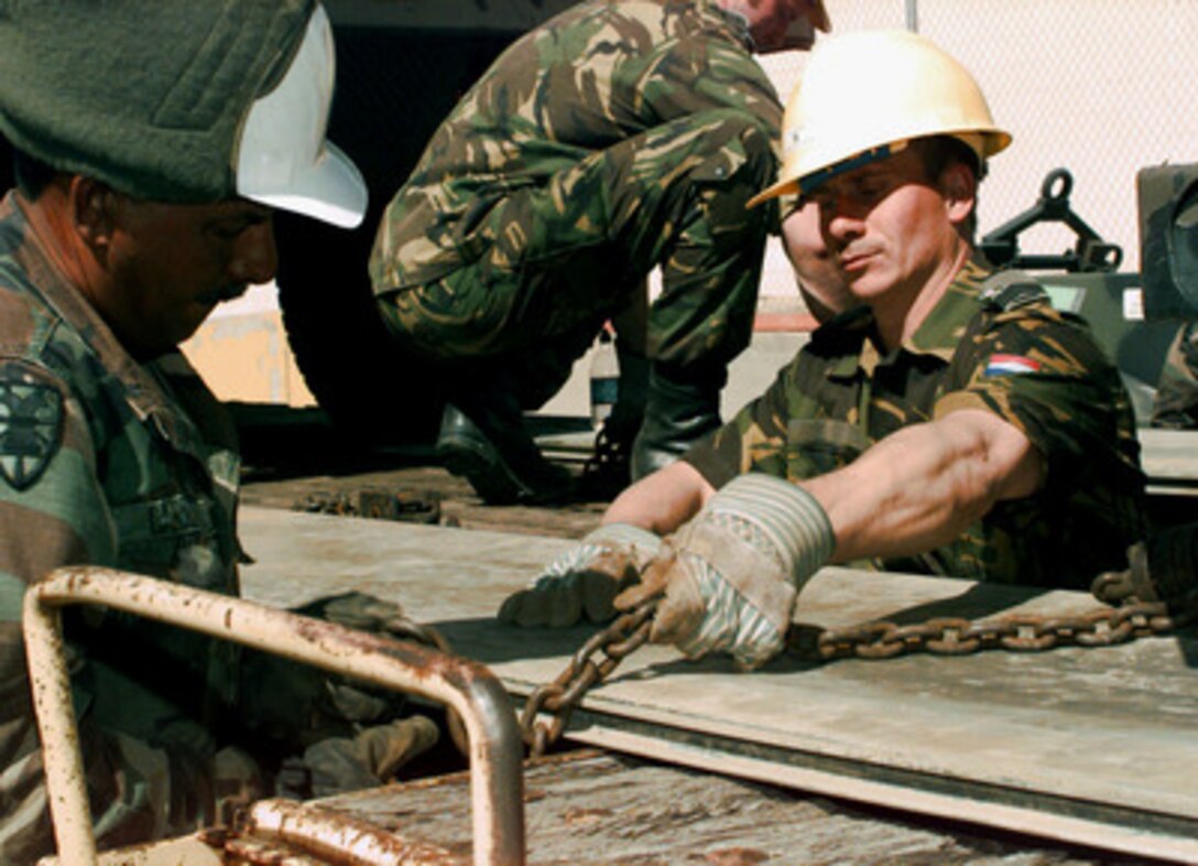 Staff Sgt. Pedro Carrillo and Sgt. Arnald A. de Jonge chain down a plank for vehicles drive over between boxcars during a train unloading at Roswell, N.M. on April 10, 1997. The train is carrying vehicles which will be used by the Netherlands Army in Exercise Roving Sands 97. More than 20,000 service members from all branches of the armed forces of the U.S., Canada, Germany, and the Netherlands are participating in Exercise Roving Sands 97. The exercise is designed to refine their skills in operations using an integrated air defense network of ground, missile and radar early warning systems combined with tactical fighter and bomber aircraft operating in a simulated high-threat environment. Carrillo is attached to the U.S. Army's 390th Transportation Company. Sgt. de Jonge is a member of the Netherlands Army. 