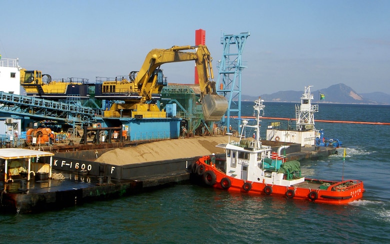 A crane transports soil from a barge onto a conveyer belt during the process of building the newly finished runway. Construction of the new runway involved the joint efforts of the government of Japan, the Ministry of Defense, the Chugoku-Shikoku Defense Bureau, the Japanese construction industry, the U.S. Army Corps of engineers, the Naval Facilities Engineering Command Pacific, the Marine Corps Air Station Iwakuni Facilities Department and others.