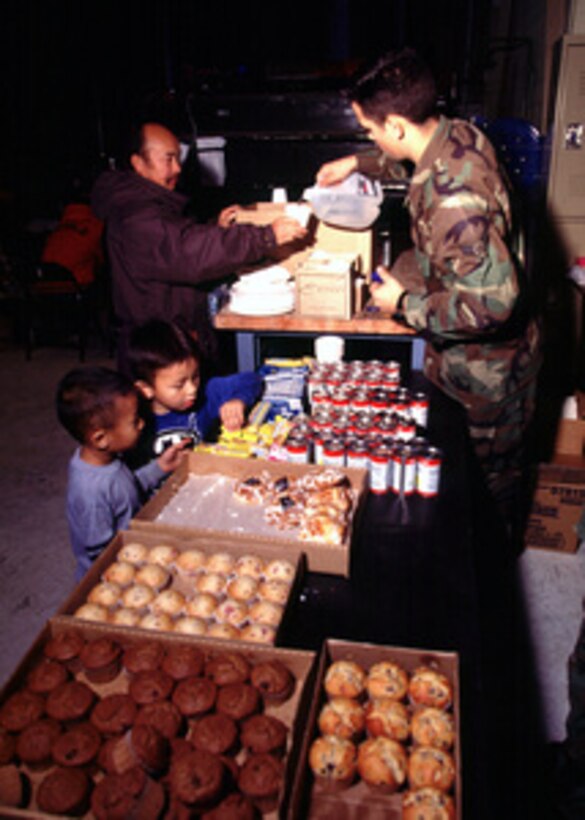 Airman 1st Class Guy Korvig (right) pours water for Chao Yang (left) inside a hangar at Beale Air Force Base, Calif., on Jan. 4, 1997. Hangars of the U.S. Air Force's 9th Reconnaissance Wing became shelters for nearly 10,000 California flood evacuees from the Yolo County area. Yang's Yuba City home was destroyed by flood waters. Korvig, a native of Boise, Idaho, is a member of the 99th Reconnaissance Squadron at Beale. 