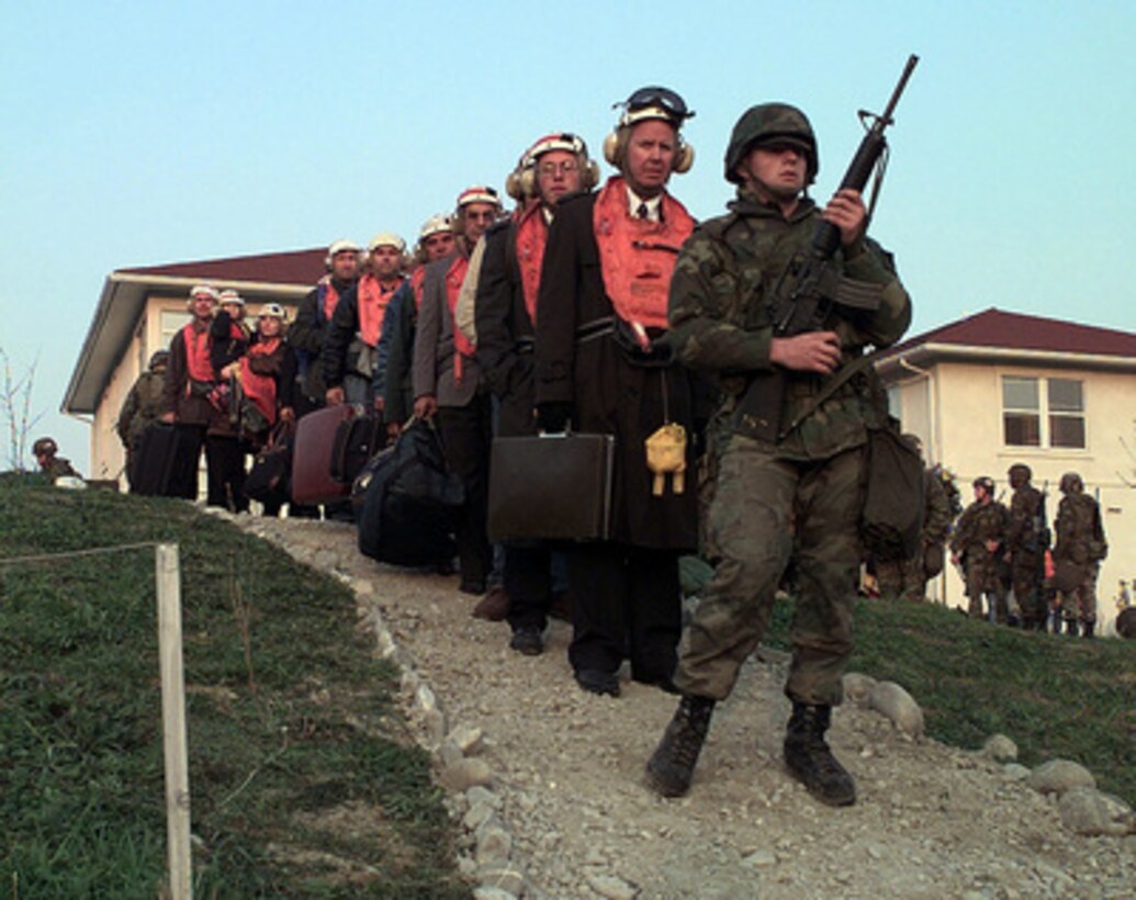 American citizens walk single-file through a heavily guarded perimeter to board a U.S. Marine Corps CH-53 Super Stallion combat assault helicopter in a field inside the U.S. Embassy housing compound in Tirana, Albania, on March 15, 1997. Operation Silver Wake is the evacuation of noncombatants from Albania to ensure the safety of American citizens and designated third country nationals. U.S. Naval forces from the USS Nassau (LHA 4) Amphibious Readiness Group continue to evacuate citizens from the U.S. Embassy in Tirana. 