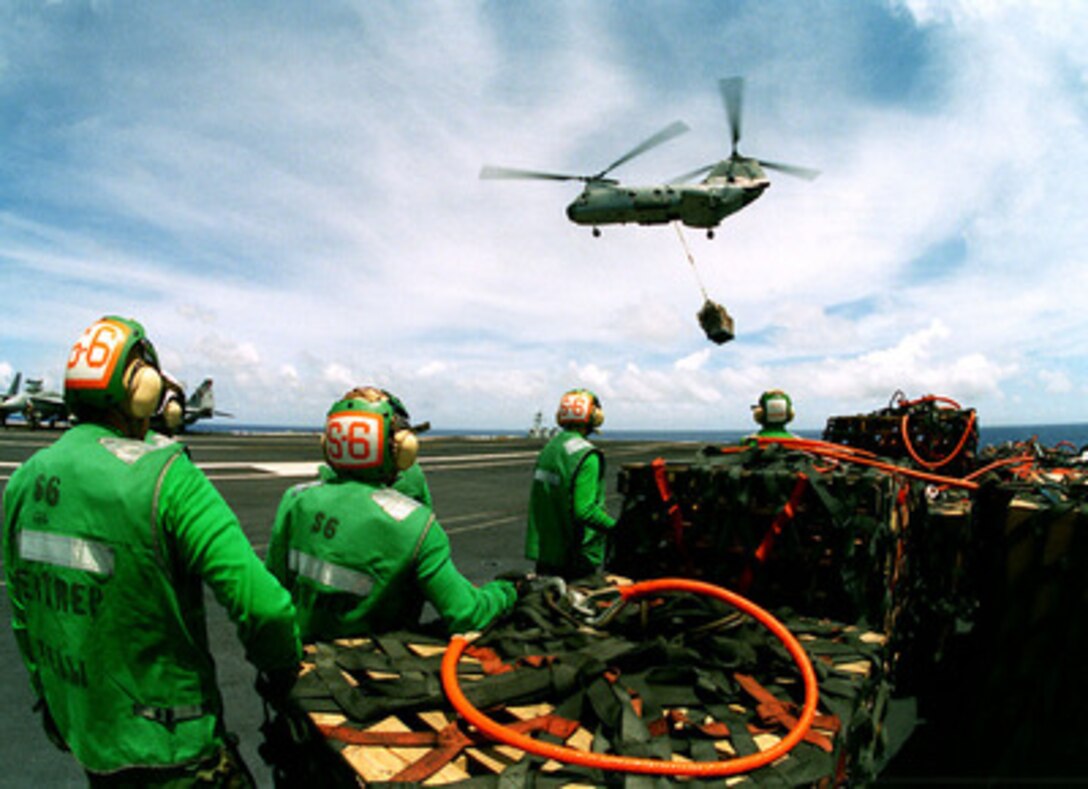 Members of the USS Constellation (CV-64) supply department watch as a CH-46 Sea Knight helicopter comes in over the flight deck with another pallet of supplies during vertical replenishment operations in the central Pacific Ocean on April 10, 1997. The Sea Knight, from Helicopter Combat Support Squadron 11, is delivering supplies from supply ships steaming in formation with the carrier. The USS Constellation battle group is en route to the Persian Gulf to enforce no-fly zones and monitor shipping to and from the region. 