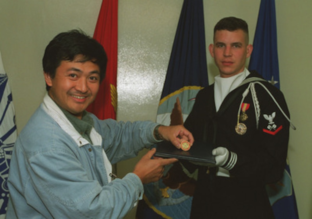 Mr. Jianyi Yang of Sichuan, China, was honored at the Pentagon, October 22, 1997, as the 130,861st visitor of the year to take a Pentagon tour -- breaking the record set in 1996. Pentagon tours were instituted during the bicentenial in 1976, and, because of there great popularity, have remained a tourist attraction ever since. In addition to receiving a special motorized tour of the world's largest office building, Mr. Yang was presented a certificate attesting to his record breaking status and a Secretary of Defense medallion. Here, Petty Officer 3d Class John Albano, presents Mr. Yang with a medallion struck especially for the Pentagon Tour Guides. 