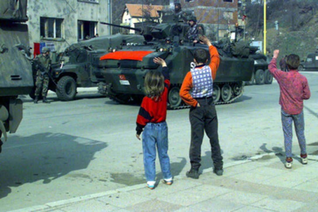 Children wave to a column of Turkish tanks passing through a village outside Vitkovici, Bosnia and Herzegovina, as they patrol the area during Exercise Dynamic Response 98 on March 29, 1998. The exercise is designed to test the capabilities of the NATO's Strategic Reserve Force in support of the in-theater Stabilization Force. 
