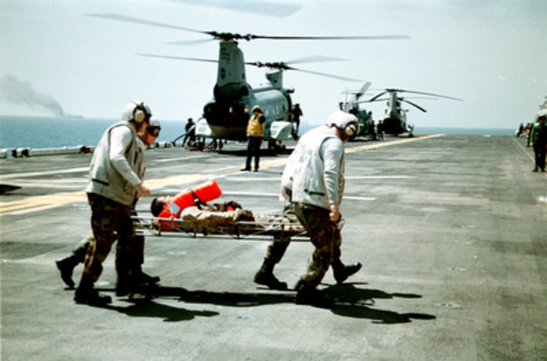 U.S. Marines from the Combat Cargo Platoon rush an injured sailor from the merchant vessel Seal-Land Mariner, seen ablaze in the background, to the medical department aboard the U.S. Navy amphibious assault ship USS Wasp (LHD 1) in the Mediterranean Sea on April 18, 1998. Search and rescue crew members, helicopters and an 18-person fire-fighting team from the Wasp responded to an emergency distress call from the merchant vessel in the Mediterranean Sea, approximately 85 miles west of Crete. A U.S. Navy CH-46 Sea Knight helicopter air-lifted two of the merchant vessel crew members to the Wasp for medical treatment of injuries caused by the initial explosion. 