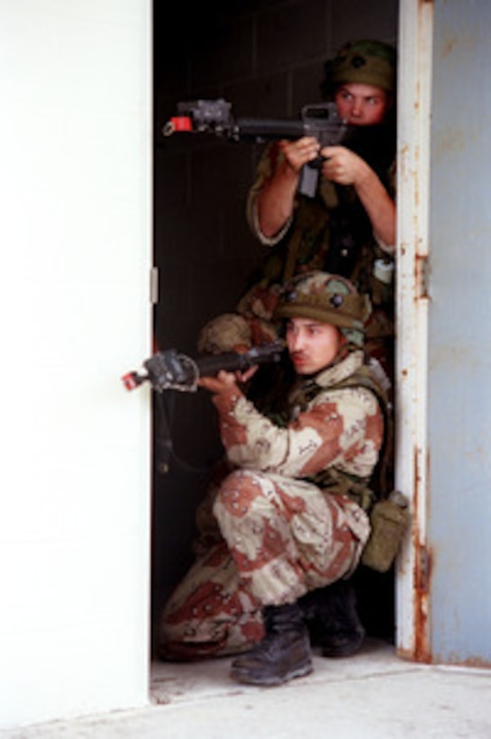 Two U.S. Marines peer out from a doorway as they maneuver their way through the Military Operations in Urban Terrain facility at Marine Corps Base Camp Lejeune, N.C., on April 22, 1998, during a rehearsal for Urban Warrior. Urban Warrior is a series of Limited Objective Experiments sponsored by the Marine Corps Warfighting Lab. The experimentation will examine the urban tactics of thrust and penetration, the use of man-portable shields and breaching technologies, and new tactical possibilities for hospital corpsmen. These Marines are attached to Bravo Company, 1st Battalion, 8th Marines. 