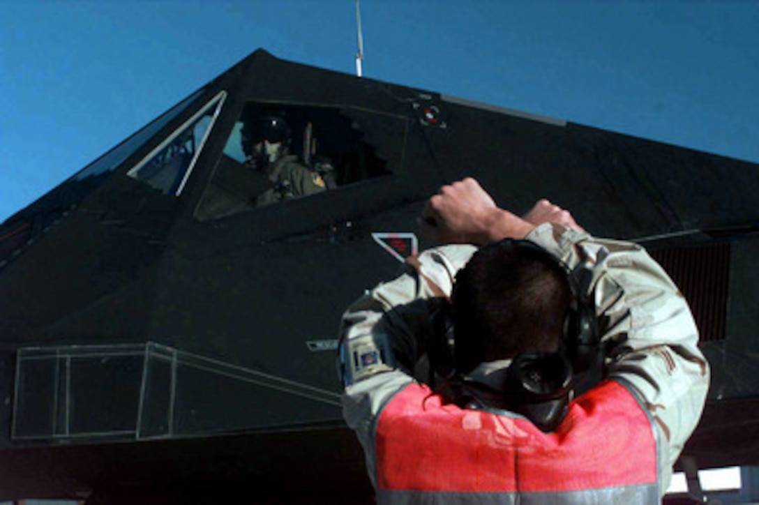 Airman 1st Class Emett Hamilton signals to Lt. Col. Doug Stewart in his F-117A Nighthawk as it parks on the ramp an operating base in Southwest Asia on Feb. 17, 1998. Stealth fighters are deploying to the Persian Gulf region in support of Operation Southern Watch. Southern Watch is the U.S. and coalition enforcement of the no-fly-zone over Southern Iraq. Hamilton and Stewart are deployed from the 8th Fighter Squadron, 49th Fighter Wing, Holloman Air Force Base, N.M. 