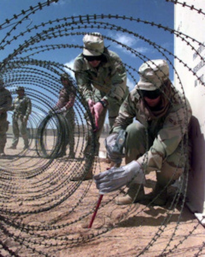 Members from the deployed security force at an operating base in Southwest Asia uncoil and stake down concertina wire around the tent city as an added measure of security on Feb. 19, 1998. U.S. Air Force personnel are operating in the Southwest Asia theater in support of Operation Southern Watch. Southern Watch is the U.S. and coalition enforcement of the no-fly-zone over Southern Iraq. 