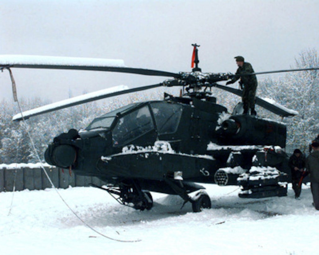 A U.S. Army soldier of the 1st Battalion 501st Aviation Brigade removes snow from the top of an AH-64A Apache attack helicopter at the Eagle Base Air Field Tuzla, Bosnia and Herzegovina, on Dec. 16, 1997. The 501st Aviation Brigade is deployed from Hanau, Germany, to Bosnia and Herzegovina to support the Stabilization Force in Operation Joint Guard. 
