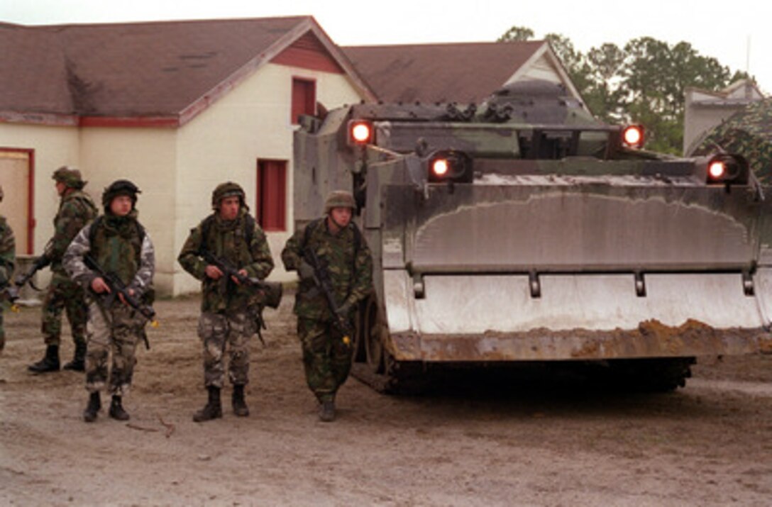 Charlie Company Marines use a M-9 Armored Combat Earthmover for cover as they patrol the medical area for role playing gang members at Camp Lejeune, N.C., on Jan. 20, 1998, during Urban Warrior. Urban Warrior is the U.S. Marine Corps Warfighting Laboratory's series of limited objective experiments examining new urban tactics and experimental technologies. The experiment is being conducted by the Special Purpose Marine Air-Ground Task Force (Experimental) from Quantico, Va., and Charlie Company, 1st Battalion, 6th Marines from Camp Lejeune. Marines from the 2nd Marine Expeditionary Force are acting as civilian role players. 