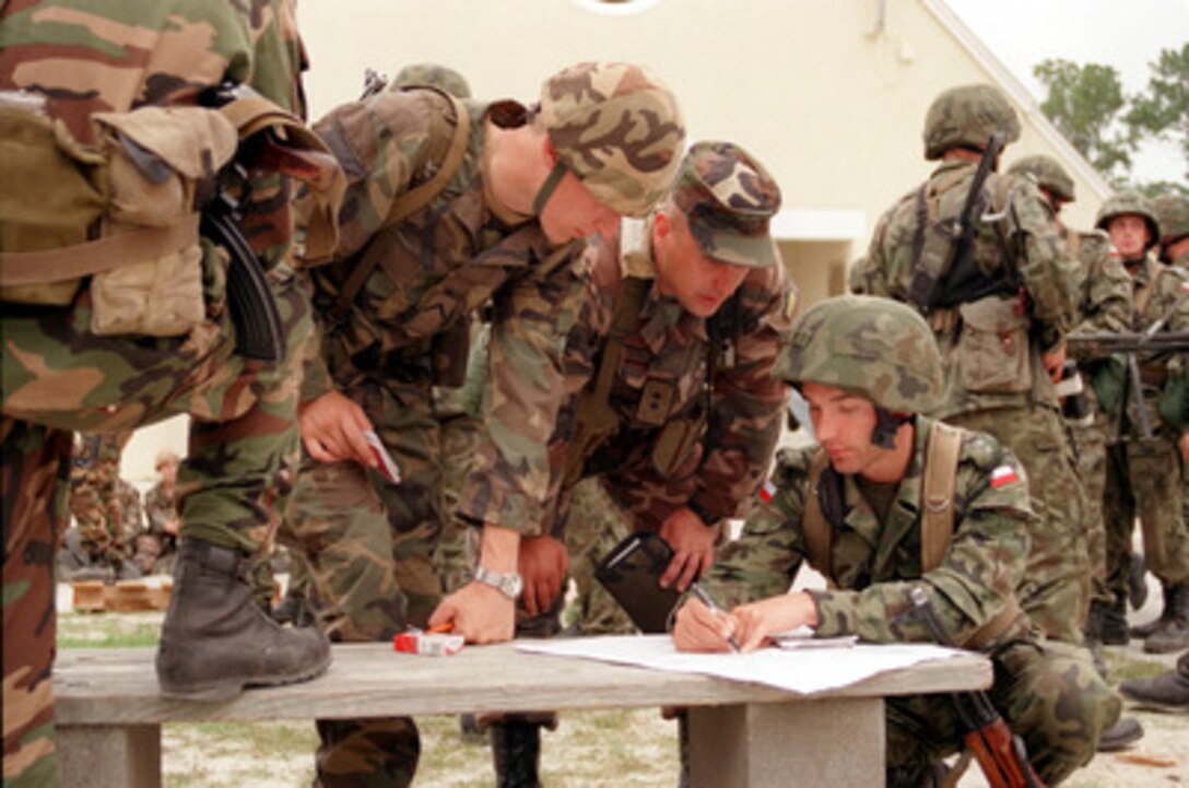 Using a bench as a desk Polish Capt. Andrzaj Stanek (right) instructs the Lithuanian soldiers of Training Company 1 on routes to patrol the streets of the Military Operations in Urban Terrain facility during Exercise Cooperative Osprey '98 on June 6, 1998, at Marine Corps Base, Camp Lejeune, N.C. Training Company 1, consisting of U.S. Marines, Polish, and Lithuanian soldiers, is being taught a wide variety of defensive and offensive urban tactics. Cooperative Osprey '98 is a Partnership for Peace situational training exercise designed to improve the interoperability of NATO and partner nations through the practice of combined peacekeeping and humanitarian relief operations. Partner nations include Albania, Bulgaria, Estonia, Georgia, Kazakstan, Kyrgyzstan, Latvia, Lithuania, Moldova, Poland, Romania, Ukraine, and Uzbekistan. Participating NATO nations include Canada, The Netherlands, and the United States. 