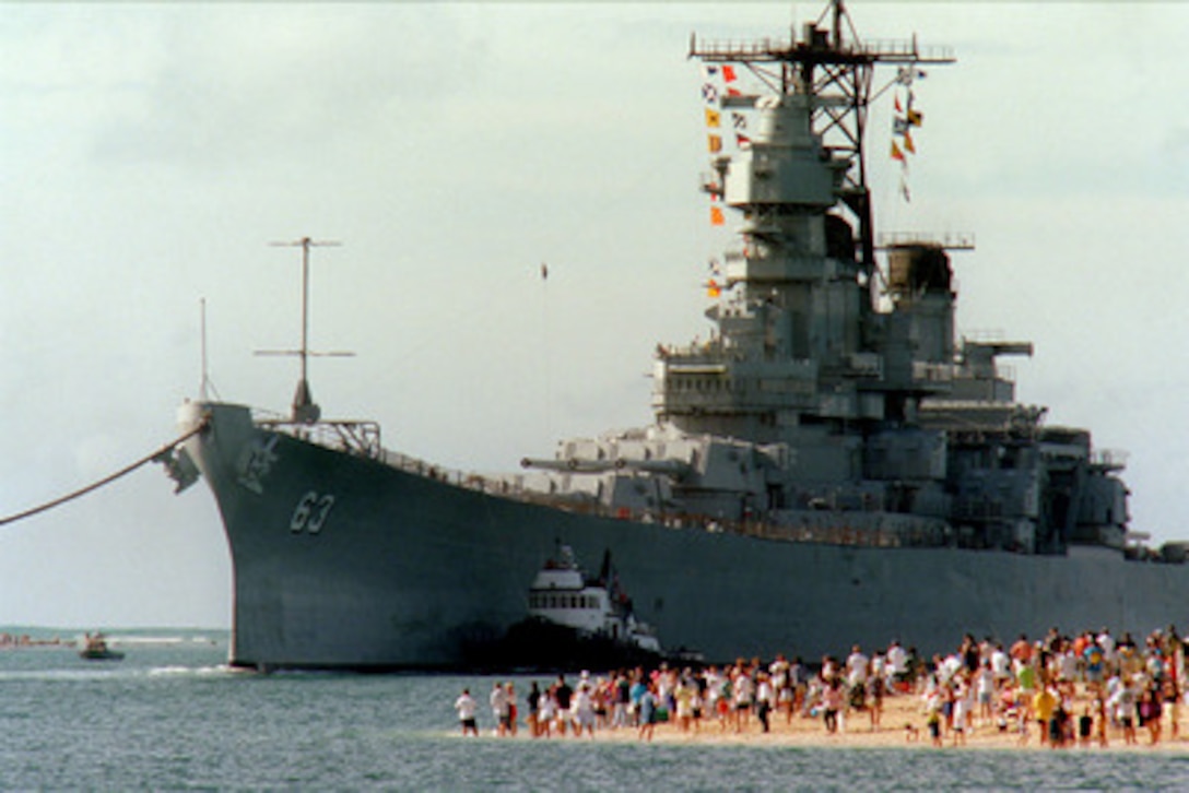 People gather on the beach to see the battleship USS Missouri (BB 63) enter the channel into Pearl Harbor, Hawaii, on June 22, 1998. Secretary of the Navy John H. Dalton signed the Donation Agreement on May 4th, allowing Missouri to be used as a museum near the Arizona Memorial. The ship was towed from Bremerton, Wash. 