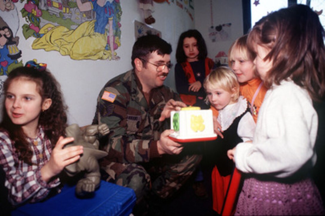 Staff Sgt. Patrick Gibbens demonstrates a toy to some of the children living at the Mother and Child Refugee Center in Simin Han, Bosnia and Herzegovina, on Jan. 30, 1998. The center houses refugees from Srebrenica, whose fathers were killed or missing from the Balkan Conflicts. Gibbens, along with members from the 401st Expeditionary Air Base Group out of Tuzla Air Base, volunteered to deliver donations of toys, food and clothing to help the people living at the refugee center. Gibbens is a U.S. Air Force ground radio repairman assigned to the 18th Eagle Air Support Operations Squadron, at Eagle Base Tuzla, Bosnia and Herzegovina, as part of the Stabilization Force in Operation Joint Guard. 