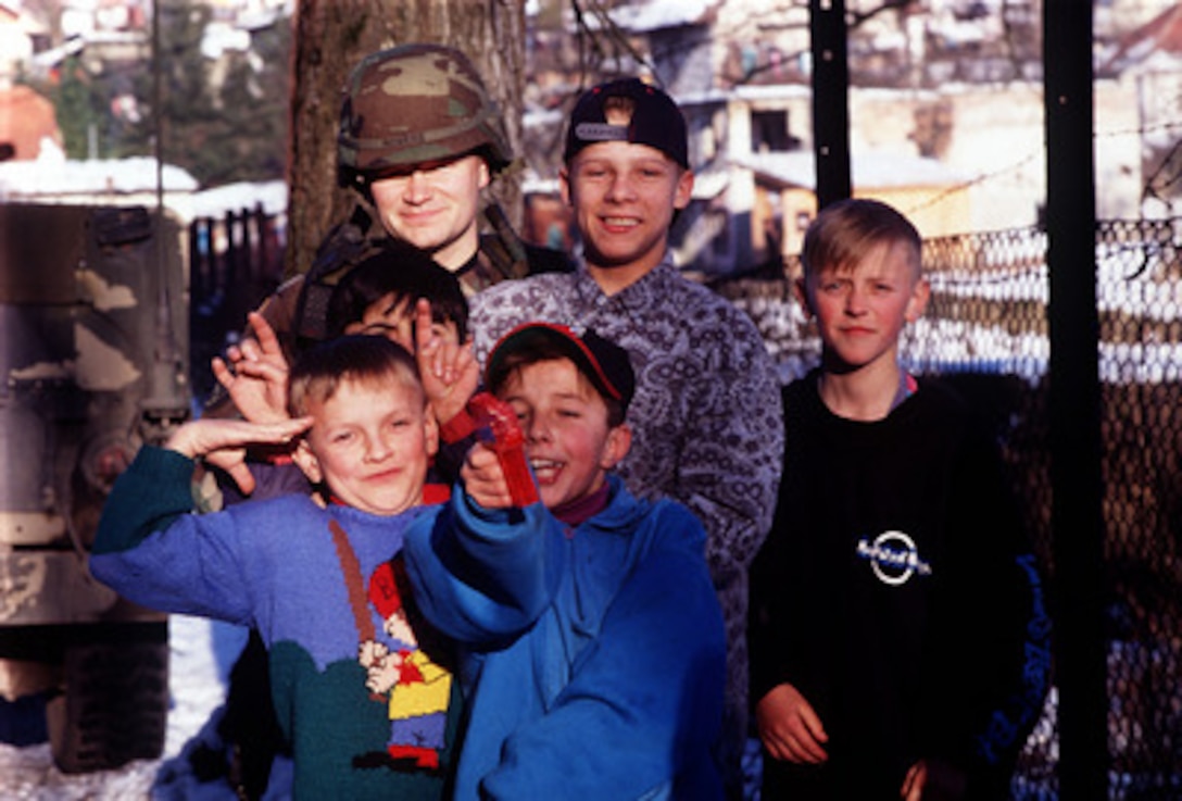 Staff Sgt. Spencer W. Rogers poses for a photo with his new found friends living at the Mother and Child Refugee Center in Simin Han, Bosnia and Herzegovina, on Jan. 30, 1998. The center houses refugees from Srebrenica, whose fathers were killed or missing from the Balkan Conflicts. Rogers, along with members from the 401st Expeditionary Air Base Group, volunteered to deliver donations of toys, food and clothing, to help the people living in the refugee center. Rogers is a U.S. Air Force security policeman from the 48th Security Forces Squadron, RAF Lakenheath, United Kingdom, assigned to the 401st Expeditionary Air Base Group Security Forces as part of the Stabilization Force in Operation Joint Guard. 