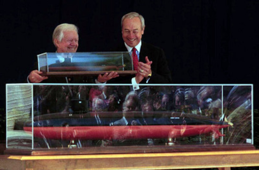 Former President and Navy submariner Jimmy Carter (left) hoists a replica of the USS Jimmy Carter (SSN 23) given to him by Secretary of the Navy John H. Dalton (right) at a naming ceremony in the Pentagon on April 28, 1998. The USS Jimmy Carter is the last of the Seawolf class submarines to be built for the U.S. Navy. 