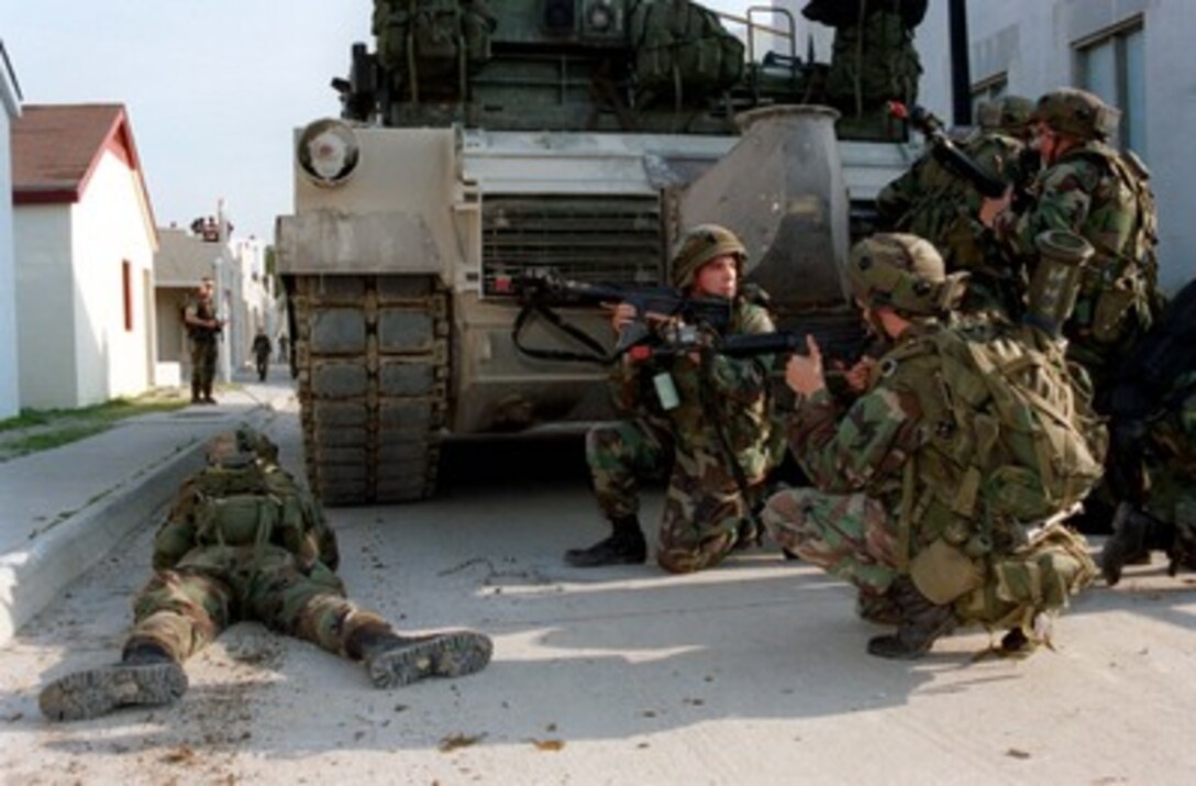 Using a tracked vehicle for cover, Marines from Bravo Company, 1st Battalion, 8th Marines, review their plan of assault at the Military Operations in Urban Terrain facility during Urban Warrior Limited Objective Exercise 2 on April 26, 1998, at Camp Lejeune, N.C. Urban Warrior is the U.S. Marine Corps Warfighting Laboratory's series of limited objective experiments examining new urban tactics and experimental technologies. 