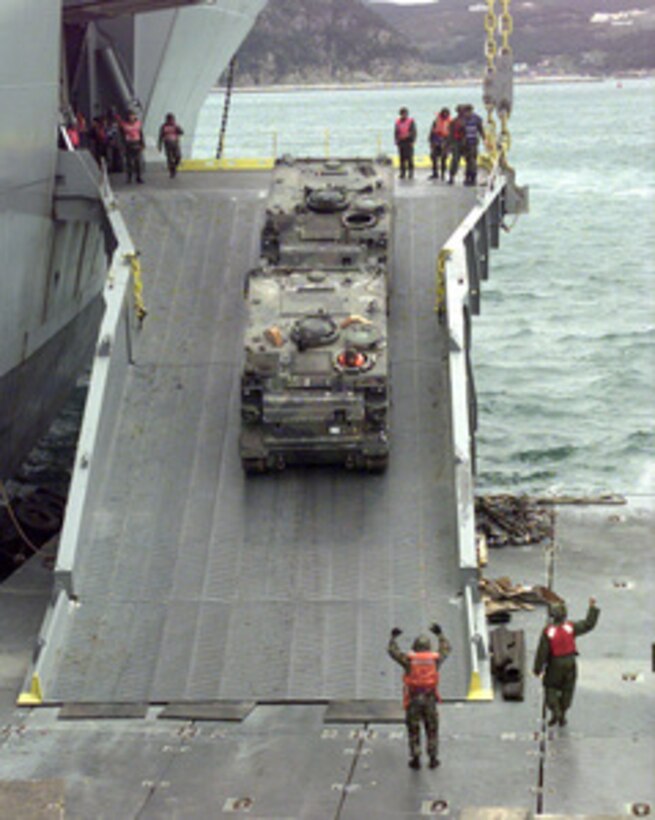 One U.S. Army M-113A2 Armored Personnel Carrier tows another down the roll-on, roll-off discharge facility of the USNS Pollux in the harbor of Pusan, Republic of Korea, on Oct. 20, 1998, for Exercise Foal Eagle '98. The ramp allows vehicles to be driven from inside the ship to a causeway and onto lighter craft for transportation to the shore. Foal Eagle '98 is a combined, joint exercise supported by forces from the U.S. and Republic of Korea. In addition to providing hands-on field experience for forces of both nations, Foal Eagle '98 was designed to test rear area protection operations and major command, control and communications systems. Pollux is one of eight Fast Sealift Ships belonging to the Military Sealift Command that have special features allowing them to load and off-load cargo in places lacking normal port facilities. 