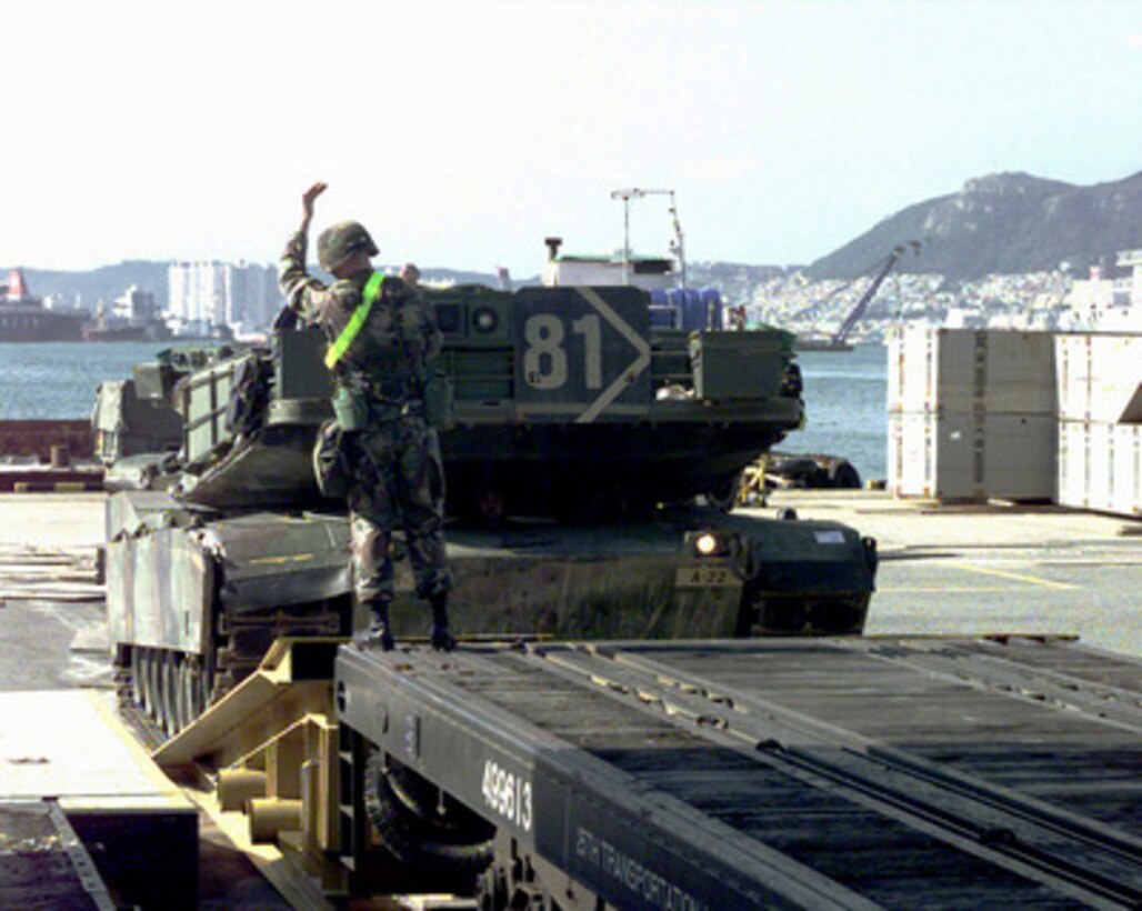 A U.S. Army soldier directs the driver of an M-1A1 Abrams Main Battle Tank onto a flat bed railroad car at the port of Pusan, Republic of Korea, on Oct. 23, 1998, for Exercise Foal Eagle '98. Foal Eagle '98 is a combined, joint exercise supported by forces from the U.S. and Republic of Korea. In addition to providing hands-on field experience for forces of both nations, Foal Eagle '98 was designed to test rear area protection operations and major command, control and communications systems. Various types of tracked vehicles are being transported by rail from Pusan to Camp Humphreys where they will link up with the rest of their contingent for the exercise. This Abrams tank comes from the 3rd Brigade, 2nd Infantry Division, Fort Lewis, Wash. 