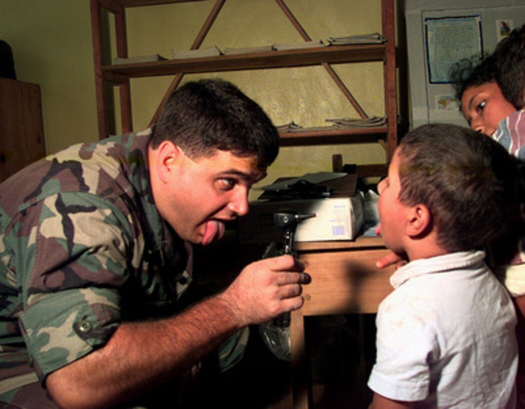 Capt. Cody L. Henderson, a U.S. Air Force pediatrician, entices a boy to stick out his tongue as he checks the boy's throat in a temporary field hospital setup by U.S. Army and Air Force medical personal in a three-room school at Campo II, Honduras, on Nov. 11, 1998. The doctors and medics drive to different villages each day and provide medical treatment for over 200 people a day. Over 1,000 U.S. service members are helping to rush food, shelter, pure water, medical aid and other relief supplies to the central Americans made homeless by Hurricane Mitch. Henderson is deployed from the 24th Medical Group, Howard Air Base, Panama. 