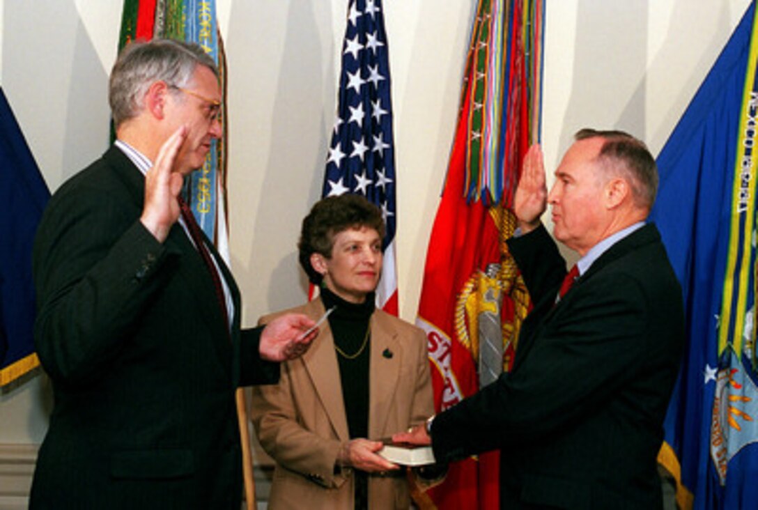 Deputy Secretary of Defense John J. Hamre (left) administers the oath of office to Jerome F. Smith Jr. (right) as the first Chancellor for Education and Professional Development in the Department of Defense while his wife Jill holds the Bible during the Pentagon ceremony on Oct. 5, 1998. 