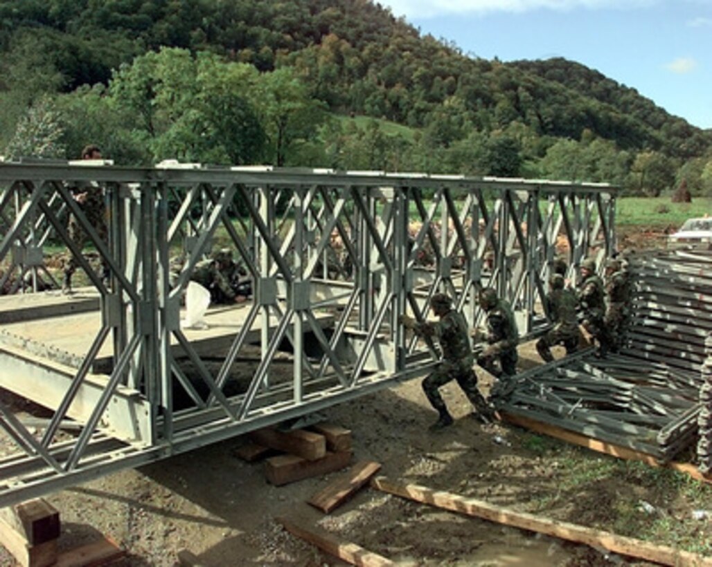 Army engineers use their brute strength to push a partially constructed Mabey and Johnson bridge into position at Camp Demi near Kladanj, Bosnia and Herzegovina, on Sept. 28, 1998. The flooding Drinjaca river damaged the supports of the present bridge leading to the American army compound which was forced to close the gate used for multi-ton vehicle traffic. The construction of the bridge is a combined effort between the U.S. Army's Alpha Company, 40th Engineers 1st Platoon of Idar Oberstein, Germany; Alpha Company 20th Engineers 2nd Platoon, of Fort Hood, Texas; Brown and Root civilian contractors and Romanian Army Engineers. The engineers are deployed to Bosnia and Herzegovina to support Operation Joint Forge. 