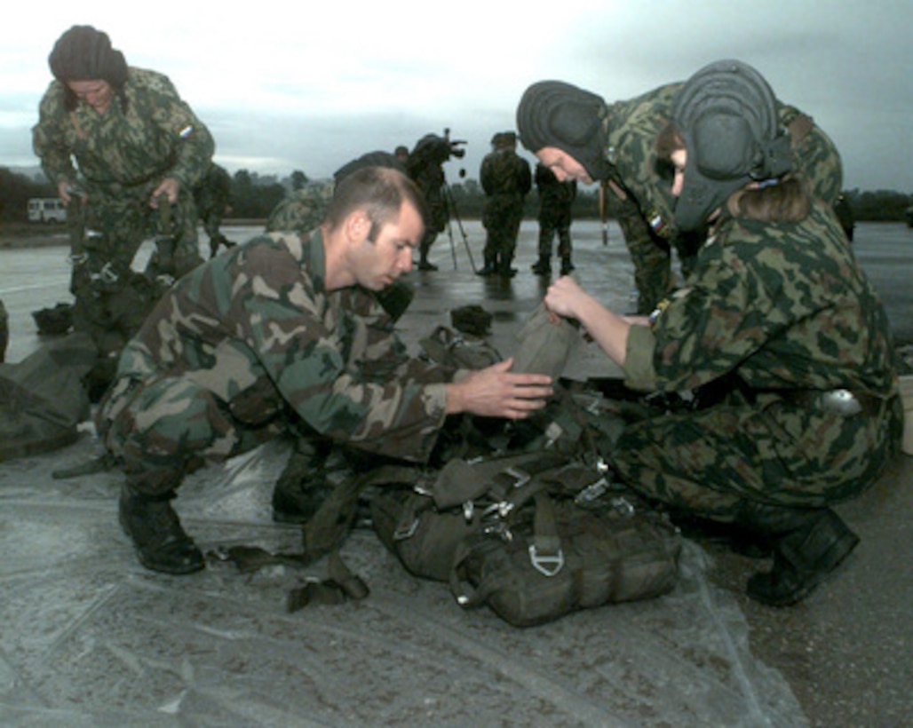 Staff Sgt. Russell Brion, U.S. Army (left), helps Russian Sgt. Helen Viliulina (right) with her parachute gear at Eagle Base, Tuzla, Bosnia and Herzegovina, on Sept. 28, 1998. Both soldiers are preparing to participate in a joint airborne exercise with Polish paratroopers of the 6th Air Assault, 16th Airborne Battalion. Sixty-four paratroopers will jump from a U.S. Air Force C-130 Hercules flown by the 67th Special Operations Squadron, RAF Mildenhall, England. Viliulina is member of the Russian Separate Airborne Brigade, Camp Ugljevik, Bosnia and Herzegovina. Brion, attached to the 10th Special Forces Group (Airborne), Stuttgart, Germany, is deployed to Bosnia and Herzegovina to support Operation Joint Forge. 