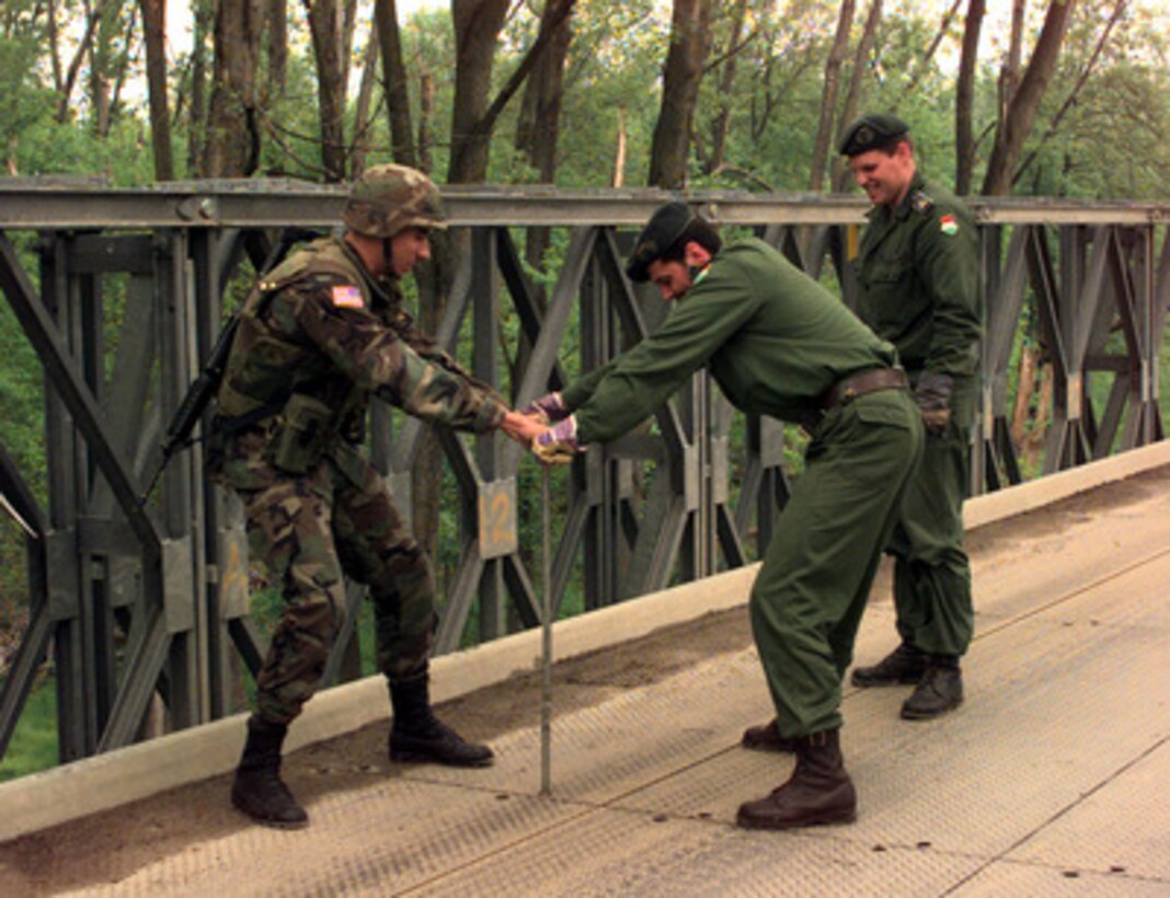 Pfc. Hector Gomez (left), U.S. Army, assists Hungarian Army Engineers in tightening a platform on the Brcko Bridge in Bosnia and Herzegovina, on April 26, 1999. Gomez is deployed to Bosnia and Herzegovina in support of Operation Joint Forge from Alpha Company, 91st Engineer Battalion, Fort Hood, Texas. 
