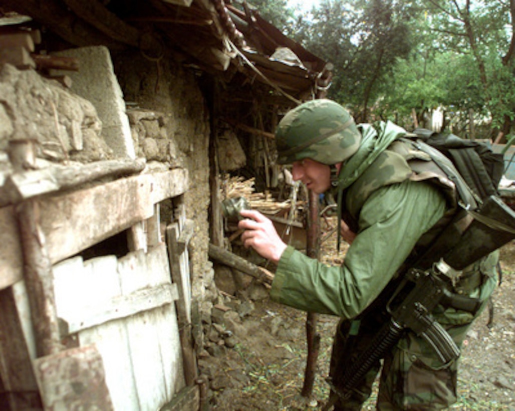 A soldier from the U.S. Army's 1st Battalion, 77th Armored Regiment peers into a shed as he searches for automatic weapons in the town of Zitinje, Kosovo, on July 26, 1999. The soldiers of the 77th are deployed to Kosovo as part of KFOR. KFOR is the NATO-led, international military force in Kosovo on the peacekeeping mission known as Operation Joint Guardian. 