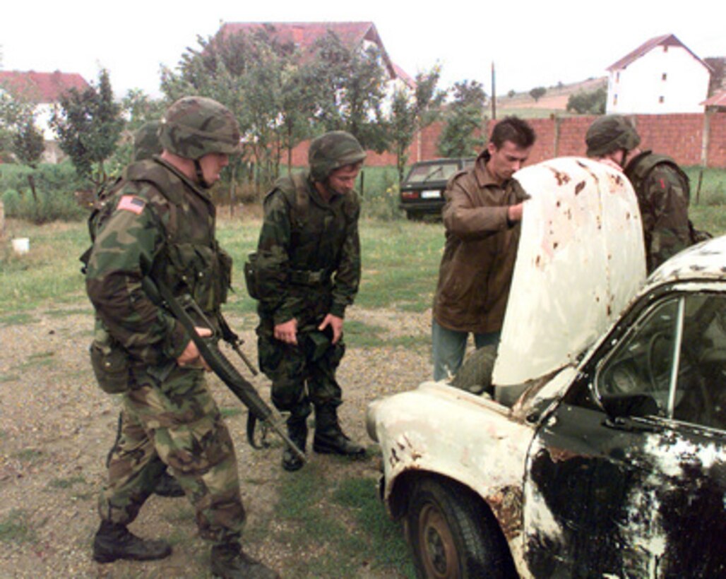 Soldiers surround a car while the owner opens the hood for inspection as they search for automatic weapons in the town of Zitinje, Kosovo, on July 26, 1999. Soldiers of the 1st Battalion, 7th Field Artillery, are deployed to Kosovo as part of KFOR. KFOR is the NATO-led, international military force in Kosovo on the peacekeeping mission known as Operation Joint Guardian. 