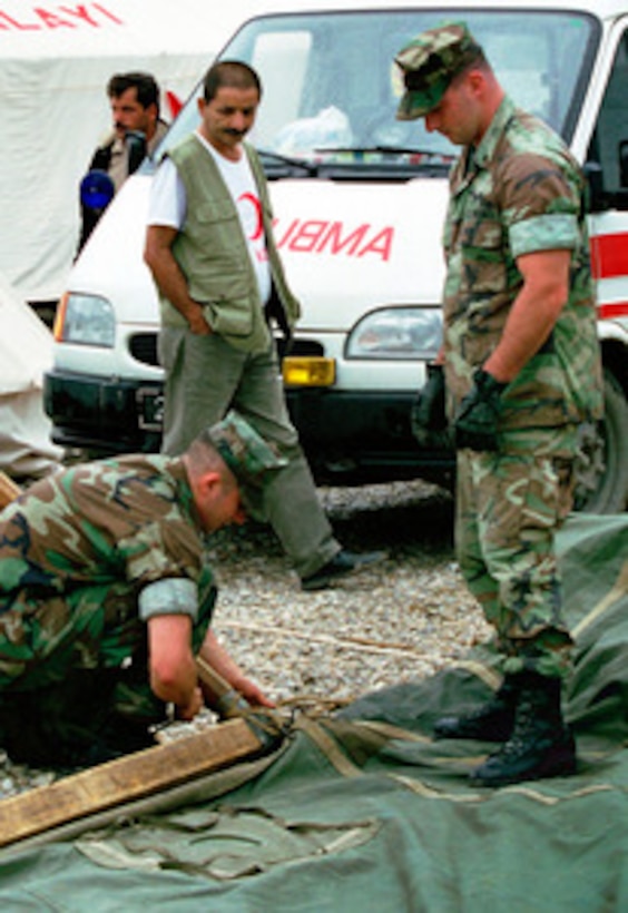 A Red Crescent Camp worker watches as U.S. Marines from the 26th Marine Expeditionary Unit prepare to put up the first of several tents at the relief camp in Degirmendere, Turkey, on Aug. 28, 1999. The Kearsarge Amphibious Readiness Group and the 26th Marine Expeditionary Unit are in Turkey to aid victims of the recent earthquake as part of Operation Avid Response. Avid Response is the U.S. military contribution to relief efforts following the earthquake that hit Western Turkey in the early morning hours of Aug. 17, 1999. 