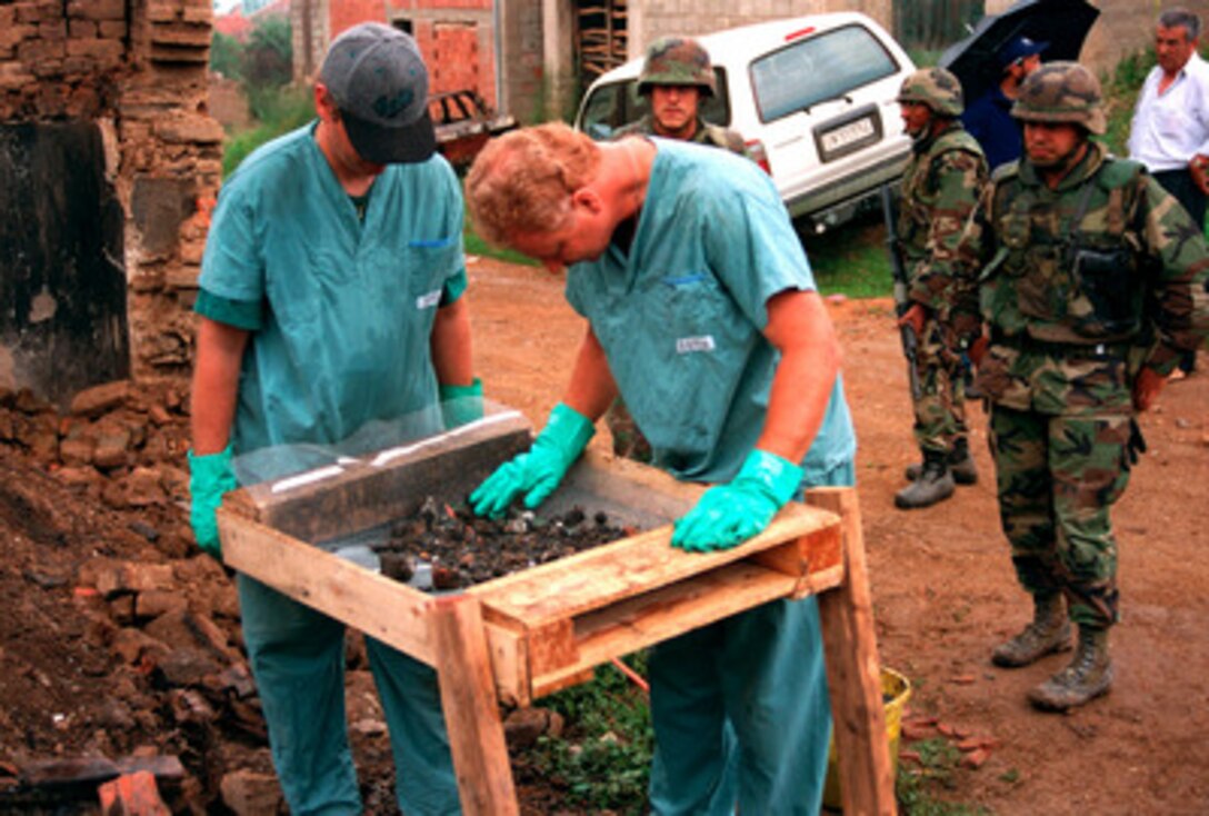 Investigators from the Royal Canadian Mounted Police Forensics Team sift through remains at a grave site in a village in Kosovo on July 1, 1999. U.S. Marines are providing security for the team as they conduct their investigation. Elements of the 26th Marine Expeditionary Unit are deployed from ships of the USS Kearsarge Amphibious Ready Group as an enabling force for KFOR. KFOR is the NATO-led, international military force which will deploy into Kosovo on a peacekeeping mission known as Operation Joint Guardian. KFOR will ultimately consist of over 50,000 troops from more than 24 contributing nations, including NATO member-states, Partnership for Peace nations and others. 