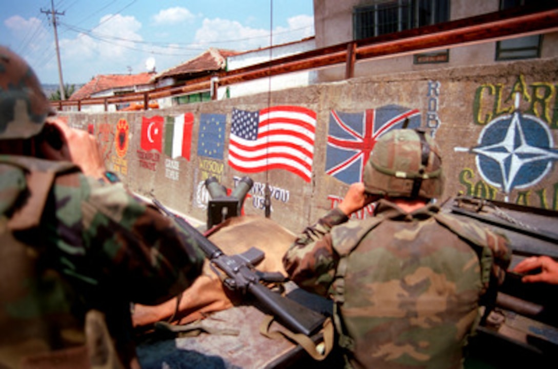 U.S. Marines from the 2nd Light Armored Reconnaissance Battalion pass flags of the NATO nations and messages of thanks painted on the retaining wall of a road in a village in Kosovo on July 5, 1999. Elements of the 26th Marine Expeditionary Unit are deployed from ships of the USS Kearsarge Amphibious Ready Group as an enabling force for KFOR. KFOR is the NATO-led, international military force which will deploy into Kosovo on a peacekeeping mission known as Operation Joint Guardian. KFOR will ultimately consist of over 50,000 troops from more than 24 contributing nations, including NATO member-states, Partnership for Peace nations and others. 