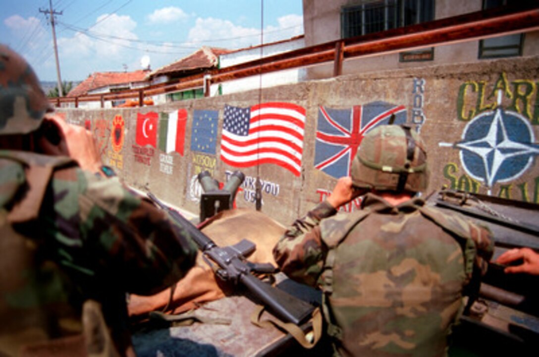 U.S. Marines from the 2nd Light Armored Reconnaissance Battalion pass flags of the NATO nations and messages of thanks painted on the retaining wall of a road in a village in Kosovo on July 5, 1999. Elements of the 26th Marine Expeditionary Unit are deployed from ships of the USS Kearsarge Amphibious Ready Group as an enabling force for KFOR. KFOR is the NATO-led, international military force which will deploy into Kosovo on a peacekeeping mission known as Operation Joint Guardian. KFOR will ultimately consist of over 50,000 troops from more than 24 contributing nations, including NATO member-states, Partnership for Peace nations and others. 