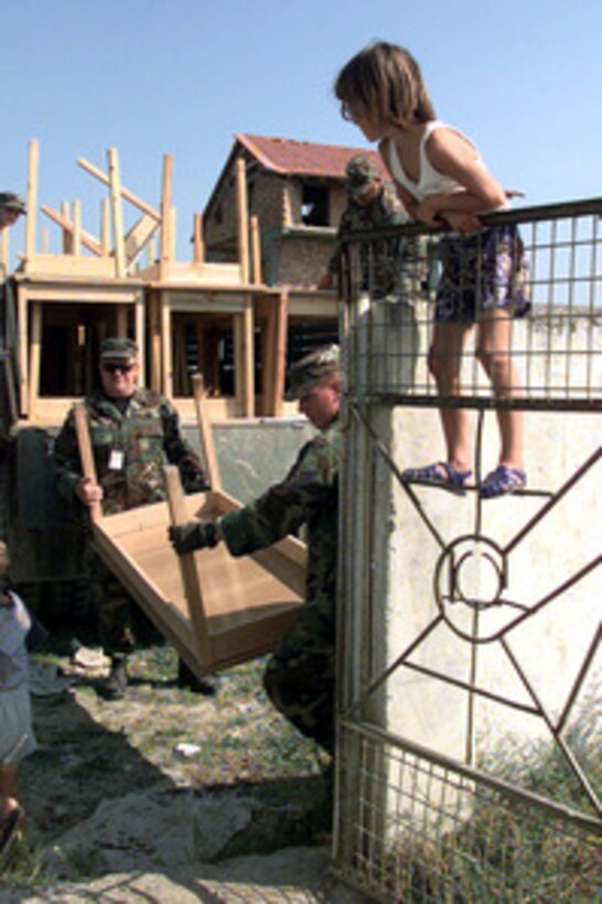 A Rinas Elementary School student watches as U.S. Air Force airmen deliver a truck full of wooden tables to the school near the Rinas Airport in Tiranë, Albania, on July 1, 1999. Servicemen and women deployed to the area have been trying to improve the conditions of local Albanian schools. 
