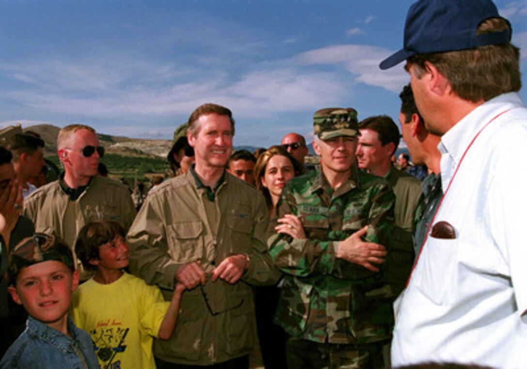 Secretary of Defense William S. Cohen (second from left) holds the hand of a refugee child as he and Supreme Allied Commander Europe Gen. Wesley Clark (right) receive a briefing from relief workers at Refugee Camp No. 1 northwest of Skopje, the Former Yugoslav Republic of Macedonia, on June 19, 1999. Cohen and Clark made a stop at the refugee camp during their visit to U.S. troops deploying for KFOR. KFOR is the NATO-led, international military force in Kosovo conducting the peacekeeping mission known as Operation Joint Guardian. 