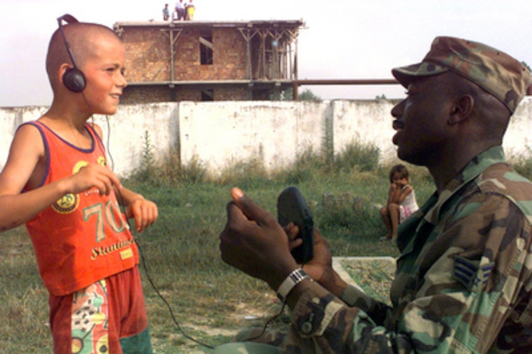 Senior Airman Justin Rhodes (right), U.S. Air Force, allows an Albanian child to listen to a compact disc player while he takes a break from his volunteer work at an elementary school in Fier, Albania, on June 12, 1999. Service men and women deployed to Albania for Operation Sustain Hope volunteered time from their day off to help clean the local elementary school which has not been repaired or maintained in years. Rhodes is attached to the 569th U.S. Forces Police Flight, Volgelweh, Germany. 