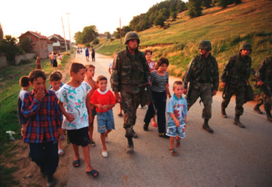 Gunnery Sgt. William Post (center) marches with the local children down the main street of Zegra, Kosovo, on June 28, 1999. Post learned from the children how to say left and right in Albanian and then proceeded to teach them how to march. Elements of the 26th Marine Expeditionary Unit are deployed from ships of the USS Kearsarge Amphibious Ready Group as an enabling force for KFOR. KFOR is the NATO-led, international military force which will deploy into Kosovo on a peacekeeping mission known as Operation Joint Guardian. KFOR will ultimately consist of over 50,000 troops from more than 24 contributing nations, including NATO member-states, Partnership for Peace nations and others. Post is attached to Lima Battery, 3rd Battalion, 10th Marine Regiment. 
