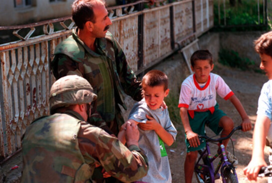A Navy hospital corpsman (left) is aided by an Albanian interpreter as he treats a young boy who has scraped his arm in Zegra, Kosovo, on June 28, 1999. The corpsman is attached to the 26th Marine Expeditionary Unit. Elements of the 26th deployed from ships of the USS Kearsarge Amphibious Ready Group as an enabling force for KFOR. KFOR is the NATO-led, international military force which will deploy into Kosovo on a peacekeeping mission known as Operation Joint Guardian. KFOR will ultimately consist of over 50,000 troops from more than 24 contributing nations, including NATO member-states, Partnership for Peace nations and others. 