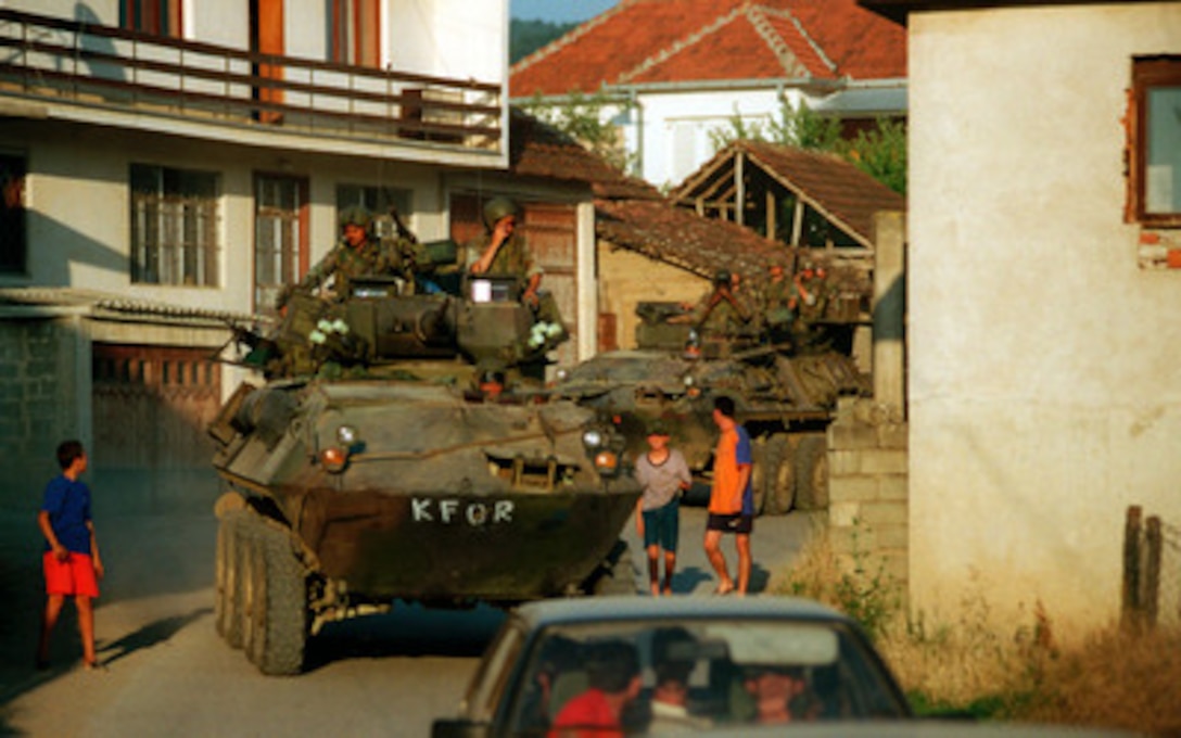 U.S. Marine Corps Light Armored Vehicles (LAV-25) escort vehicles transporting Kosovo Liberation Army members through a village in Kosovo on June 30, 1999. The KLA members were being escorted to a location where they could turn in their weapons. Elements of the 26th Marine Expeditionary Unit are deployed from ships of the USS Kearsarge Amphibious Ready Group as an enabling force for KFOR. KFOR is the NATO-led, international military force which will deploy into Kosovo on a peacekeeping mission known as Operation Joint Guardian. KFOR will ultimately consist of over 50,000 troops from more than 24 contributing nations, including NATO member-states, Partnership for Peace nations and others. The LAV's are from the 2nd Light Armored Reconnaissance Battalion. 