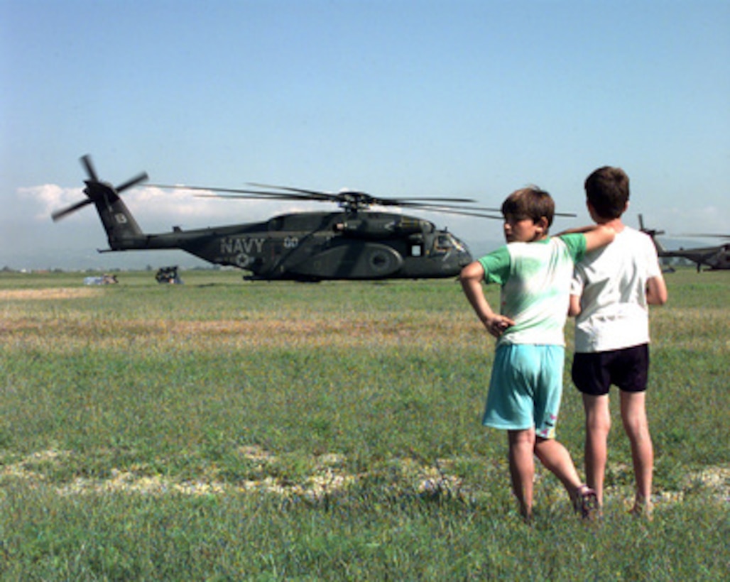 Two refugee children watch as relief supplies are unloaded from U.S. Navy MH-53E Sea Dragon helicopters at Camp Hope near Fier, Albania, on May 13, 1999, during Operation Sustain Hope. Sustain Hope is the U.S. effort to bring in food, water, medicine, relief supplies, and to establish camps for the refugees fleeing from the Former Republic of Yugoslavia. The Department of Defense has constructed Camp Hope to house up to 20,000 refugees. The Sea Dragons are airlifting in supplies from the USS Inchon (MCS 12) which is operating in the Adriatic Sea. 