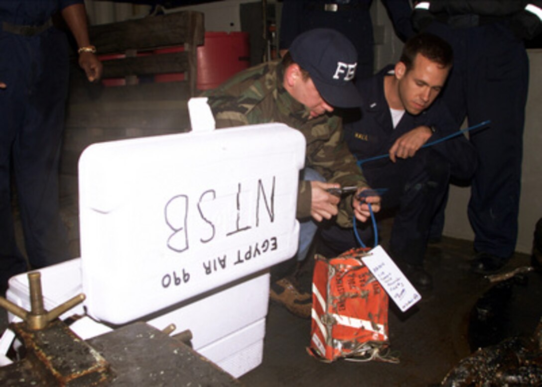 U.S. Navy Lt. j.g. Jason S. Hall (right) watches as FBI Agent Duback (left) tags the cockpit voice recorder from EgyptAir Flight 990 on the deck of the USS Grapple (ARS 53) at the crash site on Nov. 13, 1999. The flight recorder will be flown to Washington, D.C., where National Transportation Safety Board personnel will analyze the recording for clues to the plane's crash. The recorder was found by the remotely operated vehicle Deep Drone operating from the USS Grapple. 